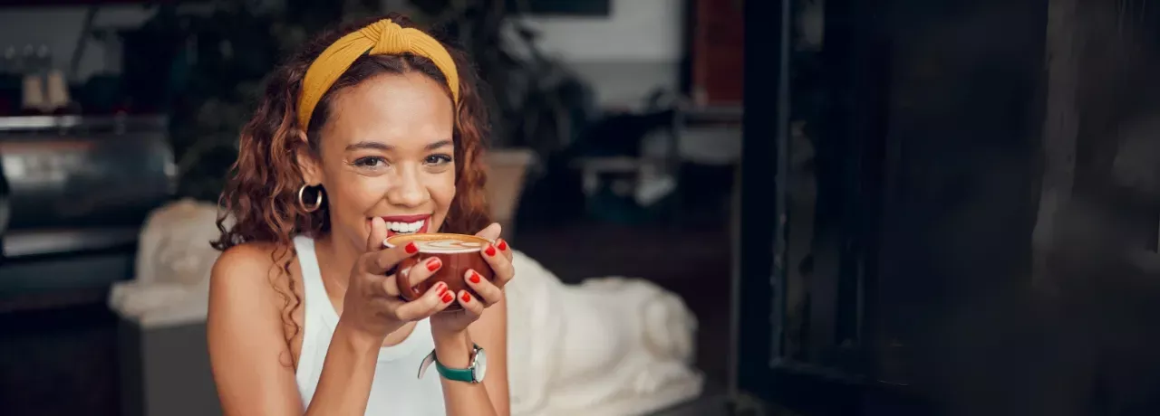 Frau lacht und hat es rote Kaffeetasse in der Hand.